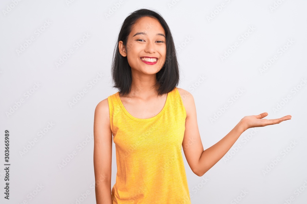 Young chinese woman wearing yellow casual t-shirt standing over isolated white background smiling cheerful presenting and pointing with palm of hand looking at the camera. Young chinese woman wearing yellow casual t-shirt standing over isolated white background smiling cheerful presenting and pointing with palm of hand looking at the camera.