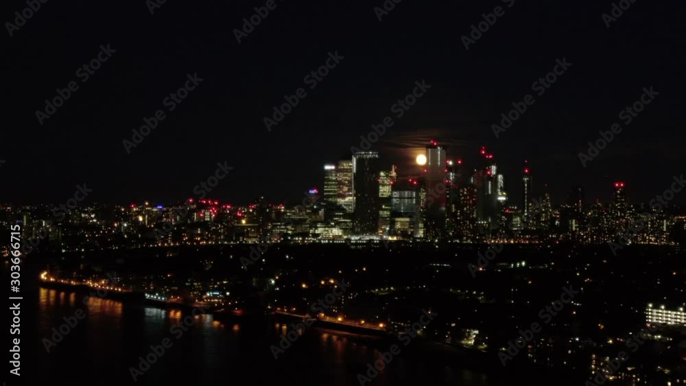 Aerial drone distant view moon rising over Canary Wharf London's Docklands Isle of Dogs and Thames River at night Aerial drone distant view moon rising over Canary Wharf London's Docklands Isle of Dogs and Thames River at night