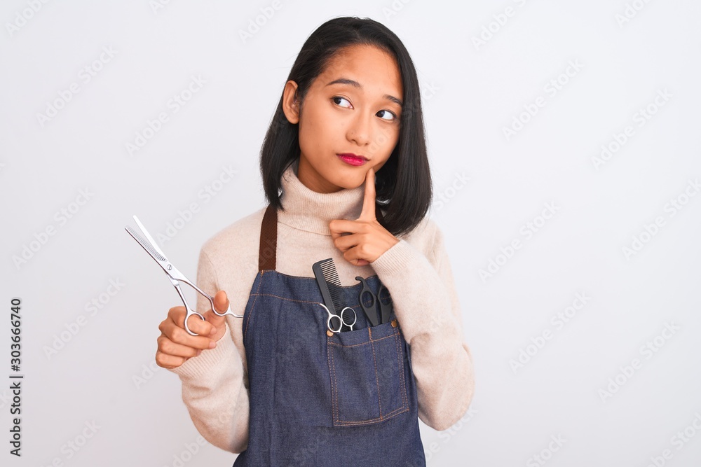 Chinese hairdresser woman wearing apron holding scissors over isolated white background serious face thinking about question, very confused idea Chinese hairdresser woman wearing apron holding scissors over isolated white background serious face thinking about question, very confused idea