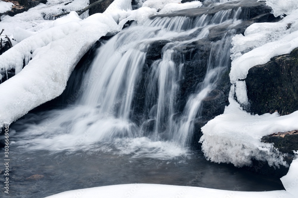 A small mountain waterfall covered in snow