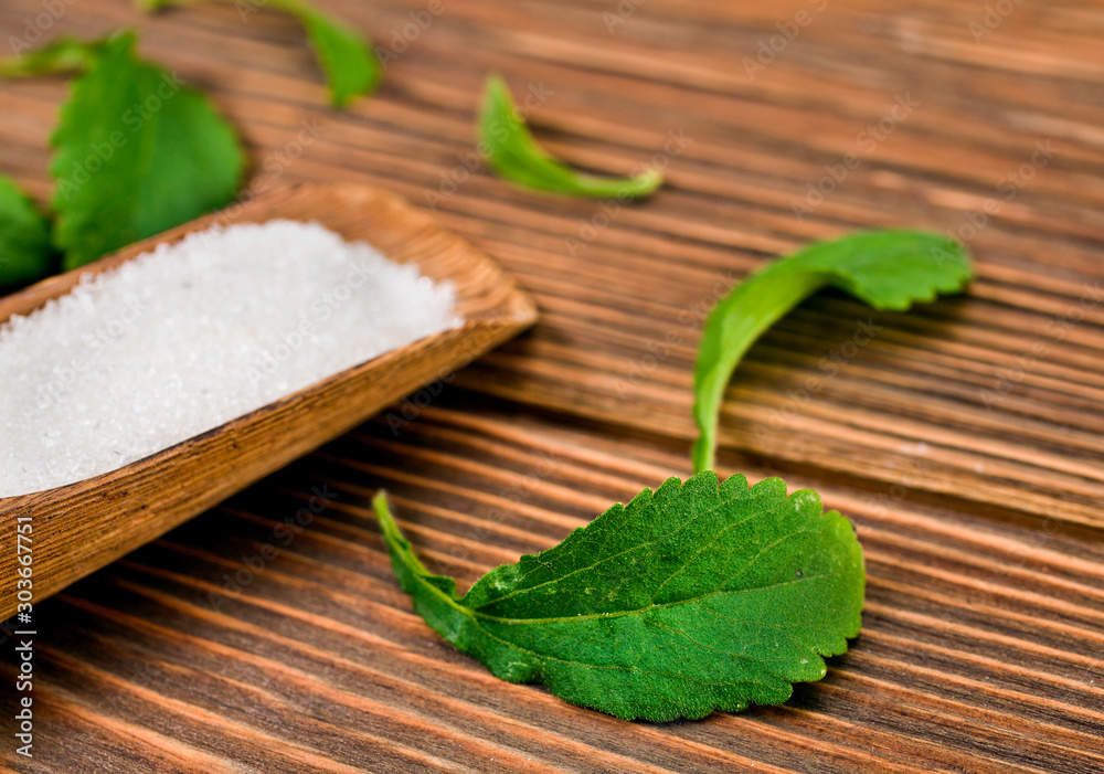 Stevia leaves with sugar in a wooden scoop on a wooden background.