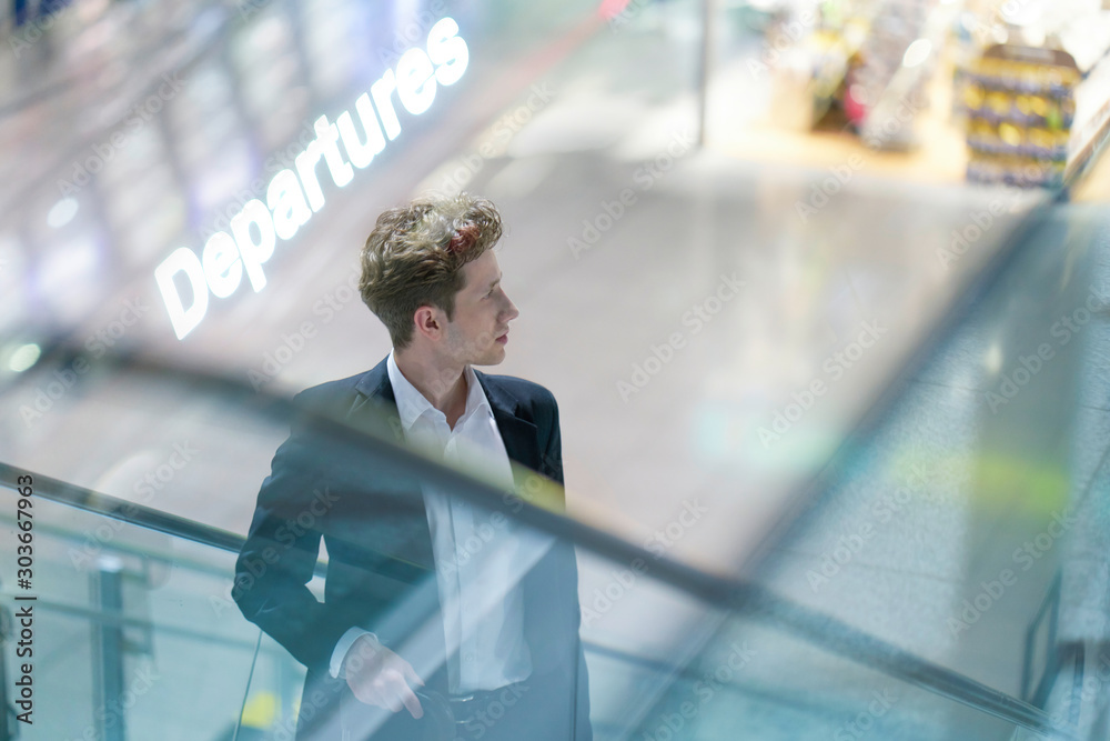Φωτογραφία Young businessman in a suit on an escalator at the airport with his luggage, uns