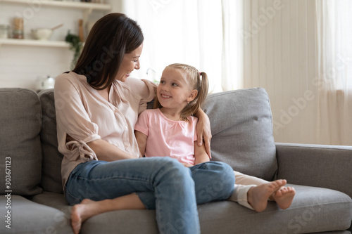 Happy young woman sitting on cozy couch with adorable daughter.