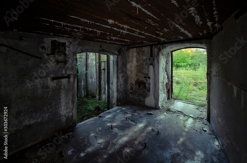 The interior of the old sea fort. Concrete side walls are available. In the doorways  green plants are visible on the street. Devastation. Background.