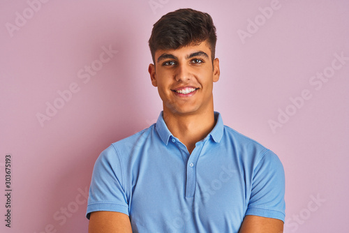 Young indian man wearing blue polo standing over isolated pink background happy face smiling with crossed arms looking at the camera. Positive person.