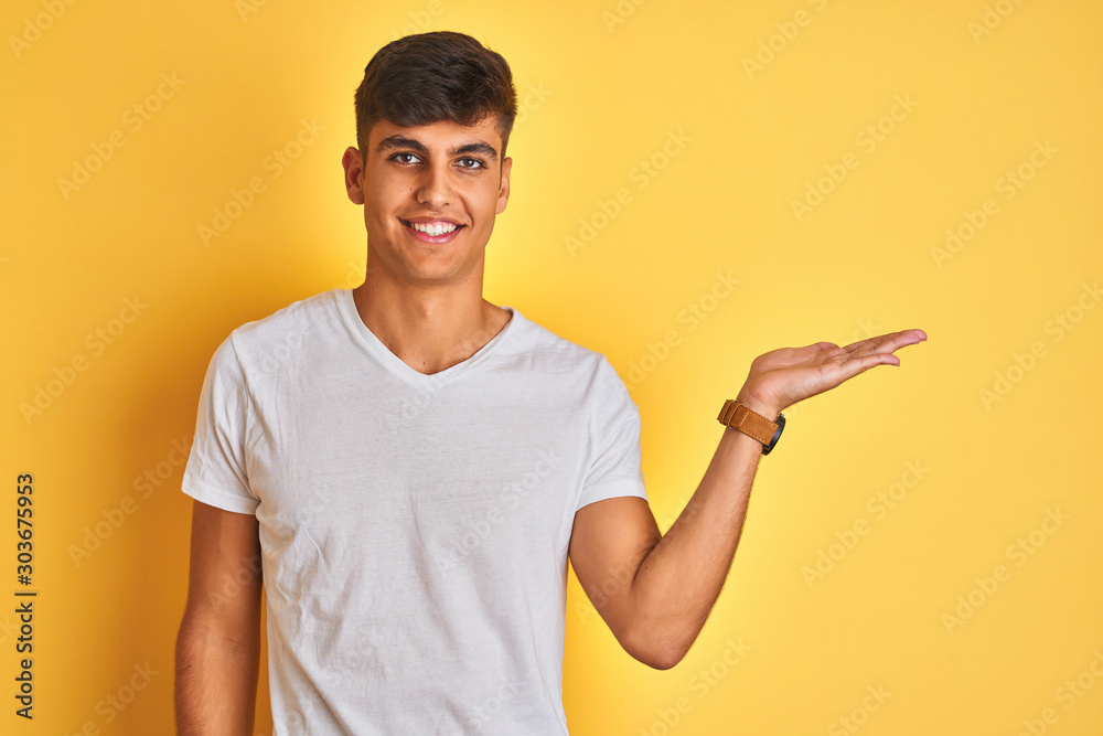 Φωτογραφία Young indian man wearing white t-shirt standing over isolated yellow background smiling cheerful presenting and pointing with palm of hand looking at the camera