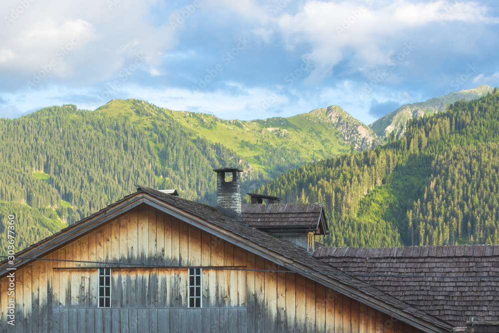 A small town at the foot of the mountains. Austrian village in a valley between the mountains. Rural landscape. Wooden roofs of houses. View of the Alps from the village. House in the mountains.