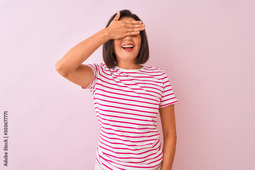 Young beautiful woman wearing striped t-shirt standing over isolated pink background smiling and laughing with hand on face covering eyes for surprise. Blind concept. Young beautiful woman wearing striped t-shirt standing over isolated pink background smiling and laughing with hand on face covering eyes for surprise. Blind concept.