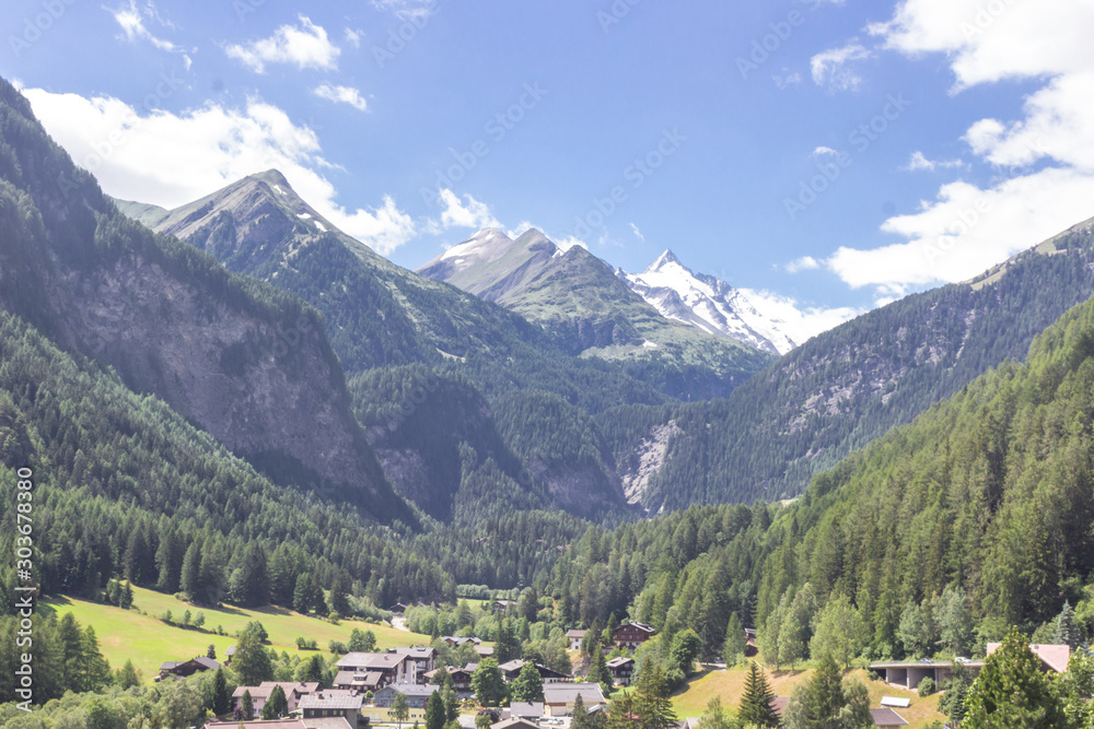 A small town at the foot of the mountains. Austrian village in a valley between the mountains. Rural landscape. Wooden roofs of houses. View of the Alps from the village. House in the mountains.