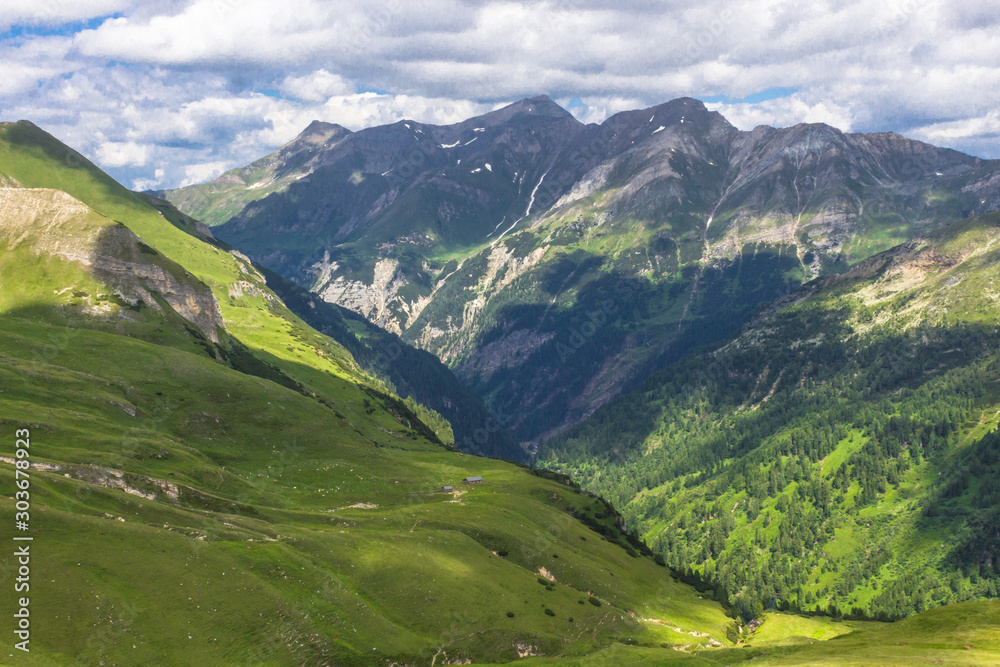 Fototapeta premium Austrian Alps. Snowy mountain peaks. Mount Grossglockner. The majesty of nature. Alpine road. Mountain landscape. Green grass in the hills. Forests among the rocks. Hiking in Europe.