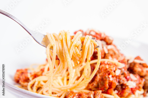 Spaghetti bolognese being eaten with a fork on a white background