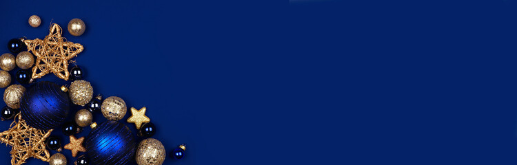 Christmas corner border banner of dark blue and gold ornaments. Overhead view on a midnight blue background.