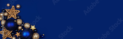 Christmas corner border banner of dark blue and gold ornaments. Overhead view on a midnight blue background.