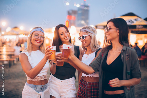 Four female friends cheering with beer at music festival