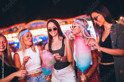 Female friends eating cotton candy and drinking beer in amusement park