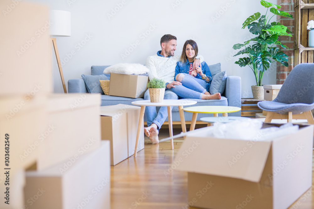 Fototapeta premium Young beautiful couple sitting on the sofa at new home around cardboard boxes