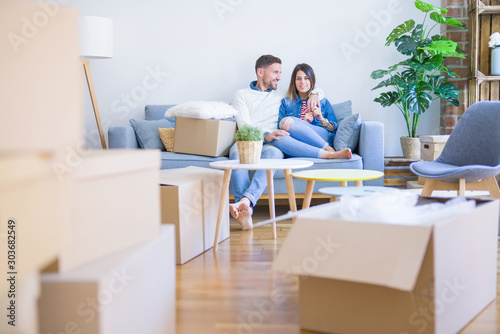 Young beautiful couple sitting on the sofa at new home around cardboard boxes