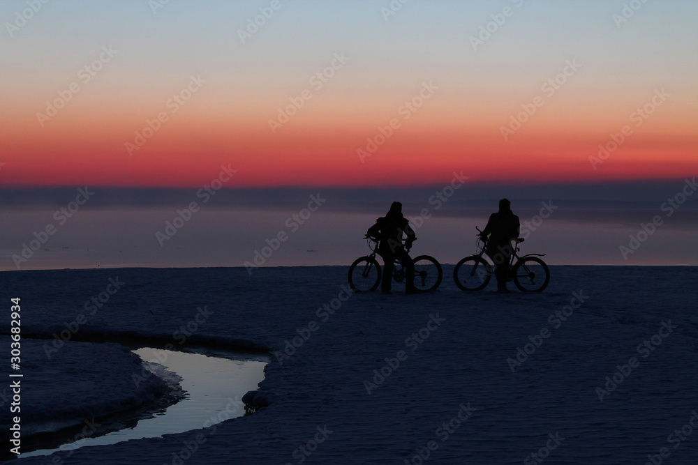 two cyclists at sunset on the ice