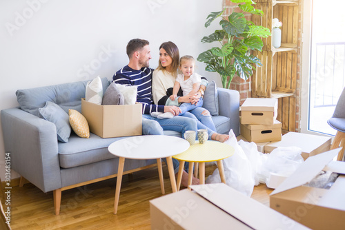 Beautiful family with kid sitting on the sofa drinking coffee at new home around cardboard boxes