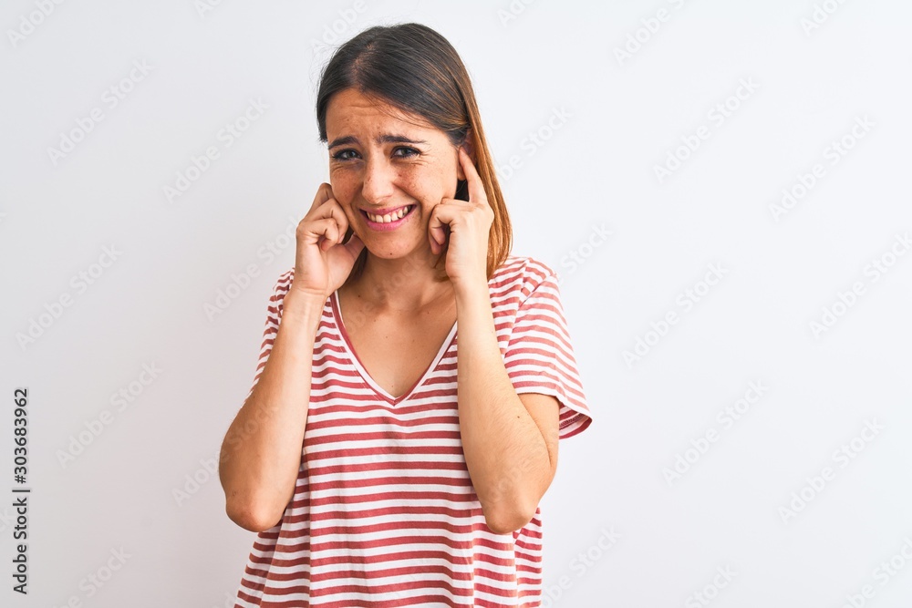 Beautiful redhead woman wearing casual striped red t-shirt over isolated background covering ears with fingers with annoyed expression for the noise of loud music. Deaf concept. Beautiful redhead woman wearing casual striped red t-shirt over isolated background covering ears with fingers with annoyed expression for the noise of loud music. Deaf concept.
