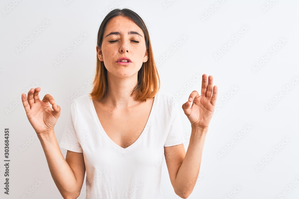Beautiful redhead woman wearing casual white t-shirt over isolated background relax and smiling with eyes closed doing meditation gesture with fingers. Yoga concept. Beautiful redhead woman wearing casual white t-shirt over isolated background relax and smiling with eyes closed doing meditation gesture with fingers. Yoga concept.