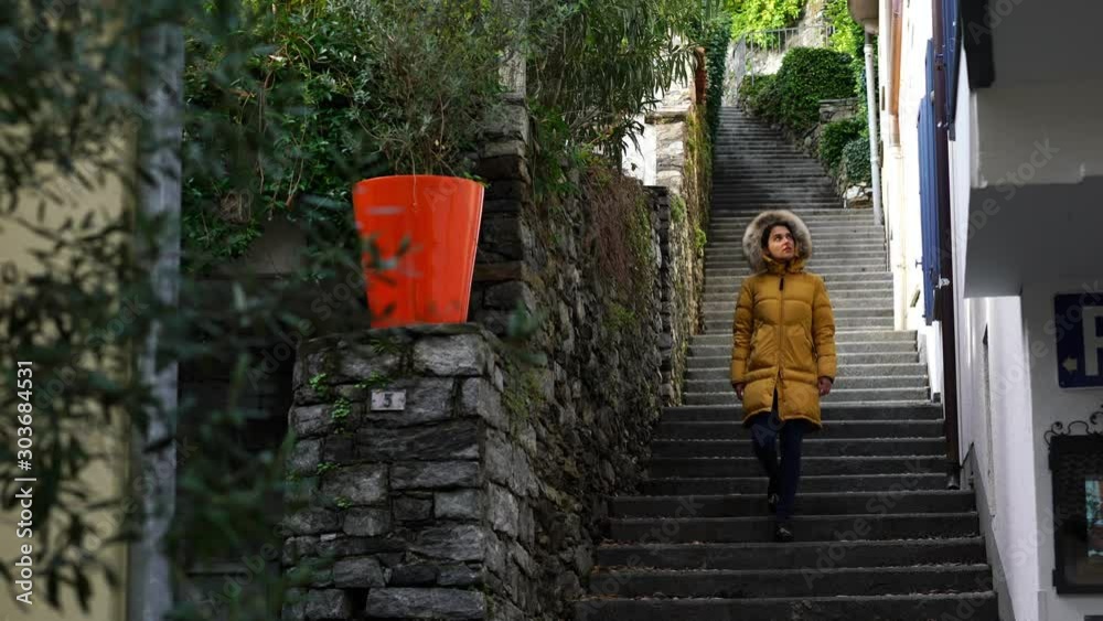 Young woman in yellow jacket descending stairs in city of Ascona, south of Switzerland. Shooting in 4K 3840 × 2160 video. Young woman in yellow jacket descending stairs in city of Ascona, south of Switzerland. Shooting in 4K 3840 × 2160 video.
