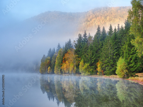 Autumn landscape in the mountains with trees reflecting in the water at St. Ana s lake  Romania