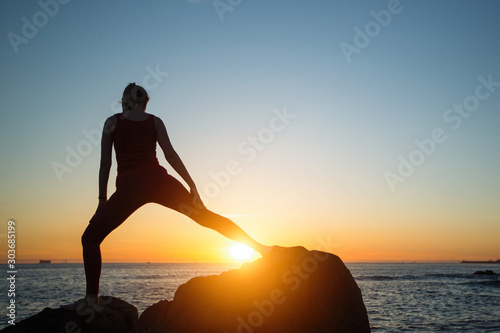 Silhouette of young yoga woman doing exercises on the ocean beach at amazing sunset. © De Visu