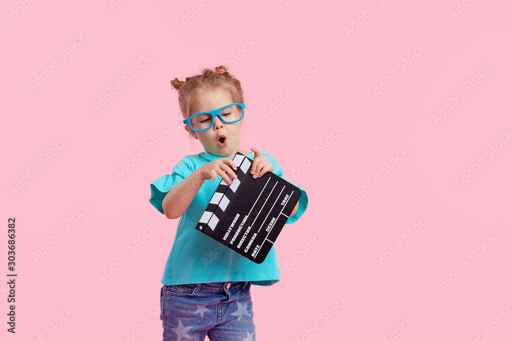 Φωτογραφία Funny smiling child girl in cinema glasses hold film making clapperboard isolated on pink background