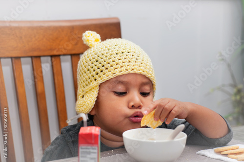 A little boy wearing a crocheted hat is playing with a bowl of soup and crackers because of loss of appetite due to illness.