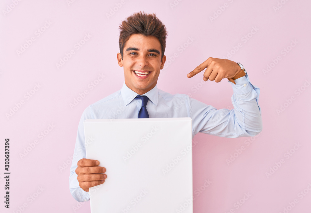 Young handsome businessman holding banner standing over isolated pink background with surprise face pointing finger to himself Young handsome businessman holding banner standing over isolated pink background with surprise face pointing finger to himself