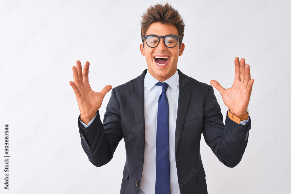 Young handsome businessman wearing suit and glasses over isolated white background celebrating mad and crazy for success with arms raised and closed eyes screaming excited. Winner concept Young handsome businessman wearing suit and glasses over isolated white background celebrating mad and crazy for success with arms raised and closed eyes screaming excited. Winner concept