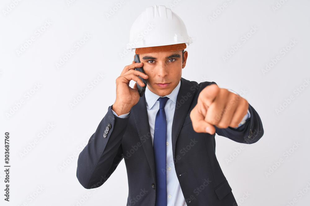Young architect man wearing helmet talking on smartphone over isolated white background pointing with finger to the camera and to you, hand sign, positive and confident gesture from the front Young architect man wearing helmet talking on smartphone over isolated white background pointing with finger to the camera and to you, hand sign, positive and confident gesture from the front