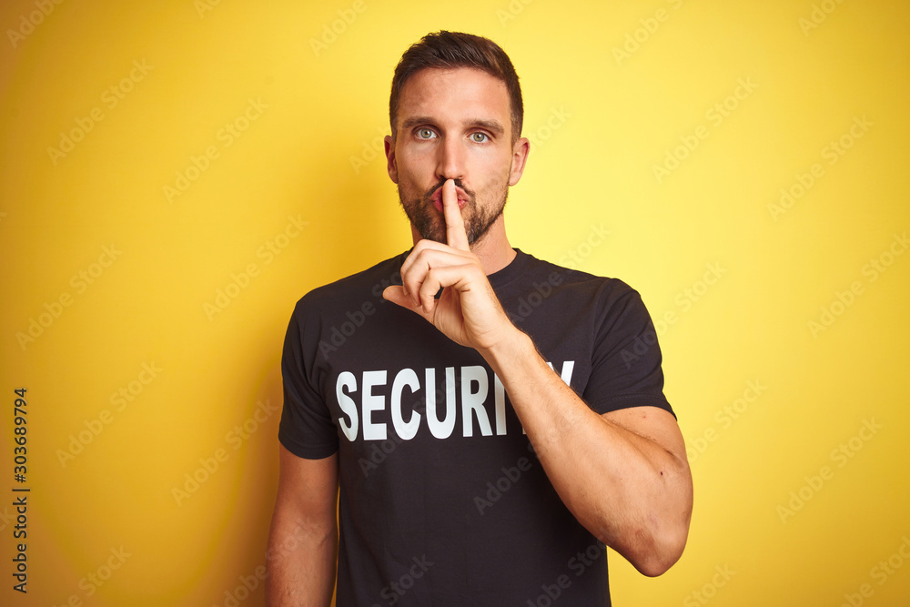 Young safeguard man wearing security uniform over yellow isolated background asking to be quiet with finger on lips. Silence and secret concept. Young safeguard man wearing security uniform over yellow isolated background asking to be quiet with finger on lips. Silence and secret concept.