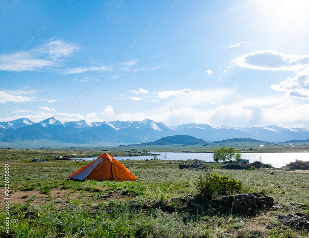 bright orange tent with blue skies and mountains and lake
