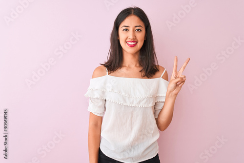 Beautiful chinese woman wearing white t-shirt standing over isolated pink background showing and pointing up with fingers number two while smiling confident and happy.