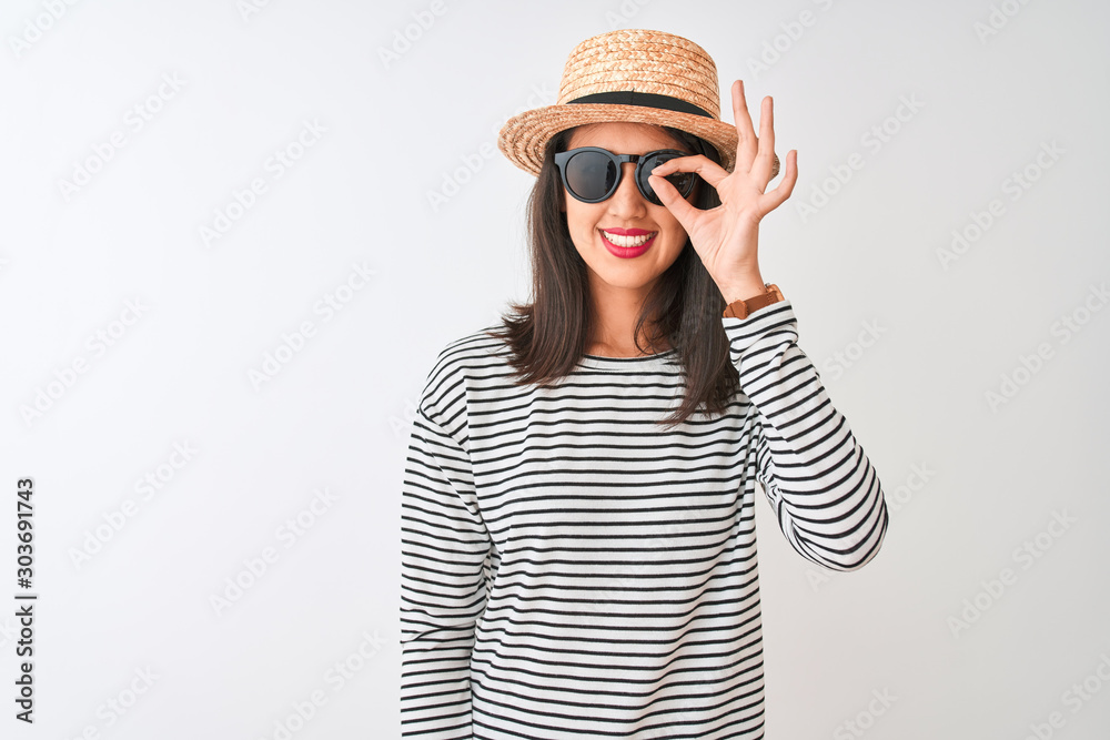 Chinese woman wearing striped t-shirt hat sunglasses standing over isolated white background doing ok gesture with hand smiling, eye looking through fingers with happy face. Chinese woman wearing striped t-shirt hat sunglasses standing over isolated white background doing ok gesture with hand smiling, eye looking through fingers with happy face.