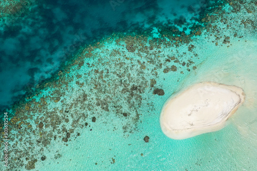 Lonely white sandbank in the middle of big ocean sea surrounded with vibrant coral reef full of marine life and crystal clear turquoise water