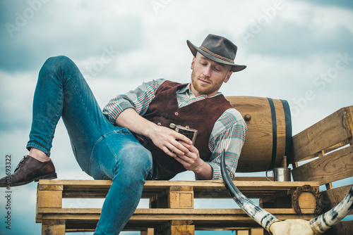 Example of true masculinity. Cowboy wearing hat. Western life. Unshaven guy in cowboy hat and plaided shirt drinking alcohol. Handsome bearded macho man. Men beauty standard.