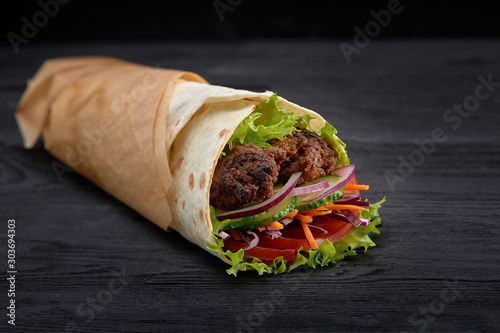 Tasty doner kebabs with fresh salad trimmings and shaved roasted meat served in tortilla wraps on brown paper as a takeaway snack photo