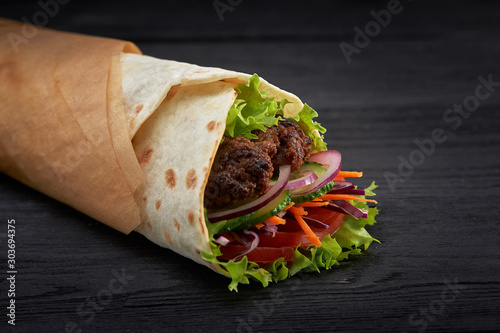 Tasty doner kebabs with fresh salad trimmings and shaved roasted meat served in tortilla wraps on brown paper as a takeaway snack