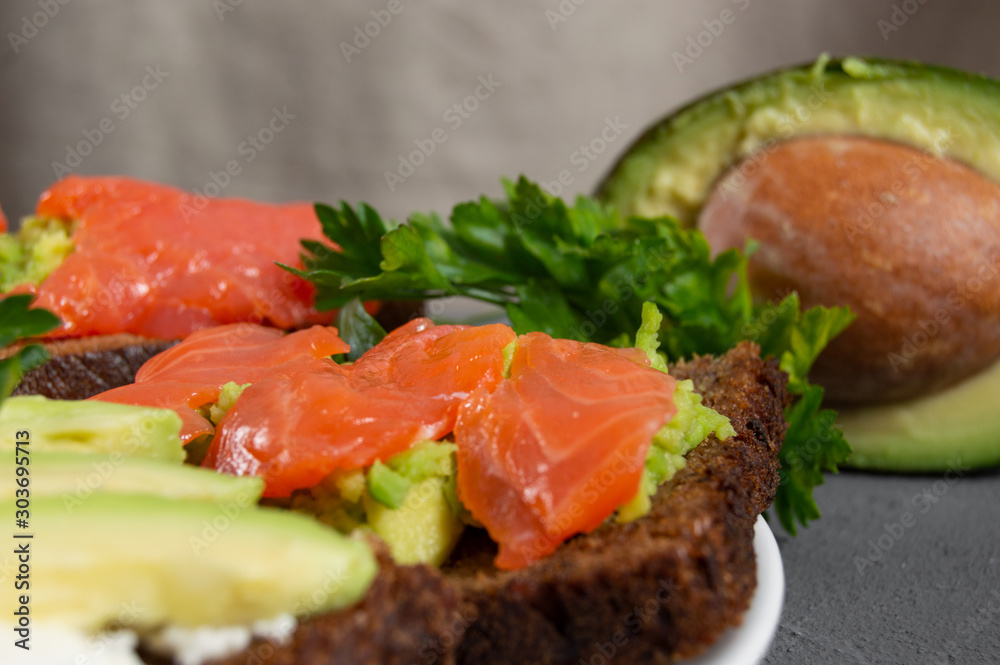 Toast with red fish trout and mashed avocado with parsley and slice avocado on background Toast with red fish trout and mashed avocado with parsley and slice avocado on background