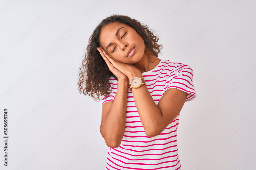 Young brazilian woman wearing pink striped t-shirt standing over isolated white background sleeping tired dreaming and posing with hands together while smiling with closed eyes.