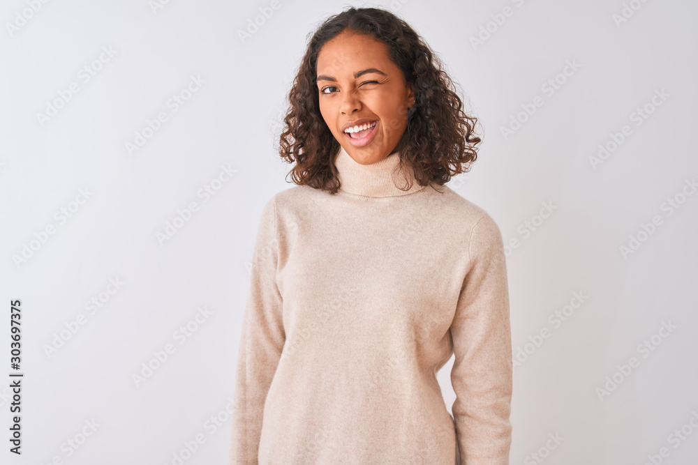 Young brazilian woman wearing turtleneck sweater standing over isolated white background winking looking at the camera with sexy expression, cheerful and happy face. Young brazilian woman wearing turtleneck sweater standing over isolated white background winking looking at the camera with sexy expression, cheerful and happy face.
