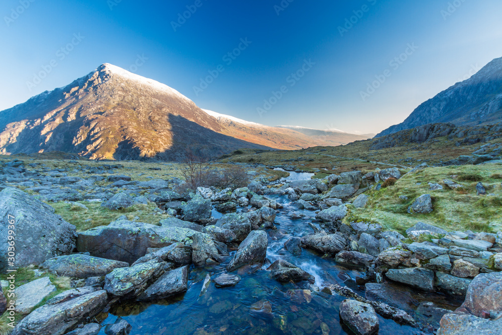 Early morning light and shadow over mountains and snow. Stream  in foreground and mountain  Carnedd Llewelyn. Landscape