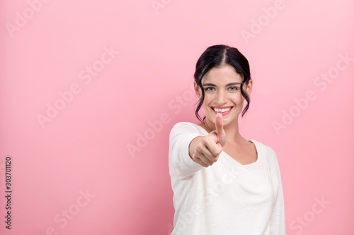 Young woman giving thumb up on a pink background