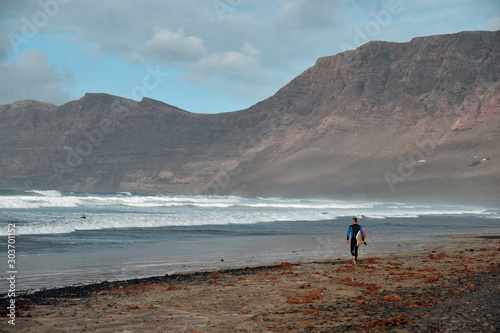 Surfers (not recognisable) on Famara beach, Lanzarote with dramatic cliffs in background