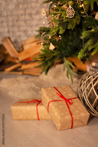 New year's gifts and wicker basket under beautiful Christmas-tree with fireplace hearth and grey brick wall background.