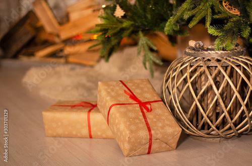 New year's gifts and wicker basket under beautiful Christmas-tree with fireplace hearth and grey brick wall background.