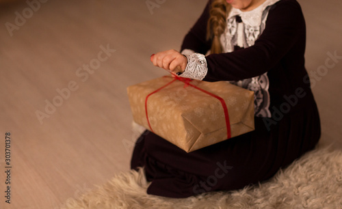 Girl in a burgundy lace retro dress opens Christmas gift